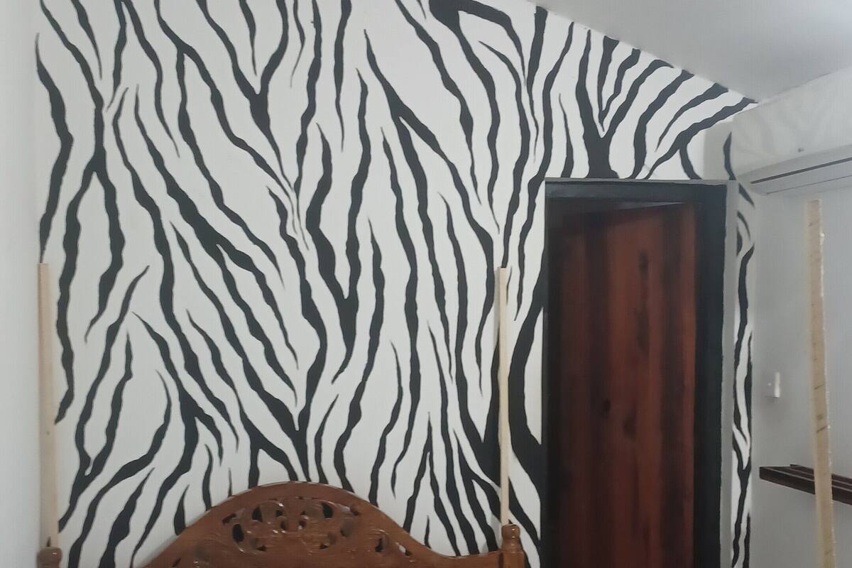 A bedroom with a zebra-striped wall, a wooden bed frame, and a blue-striped bedspread.
