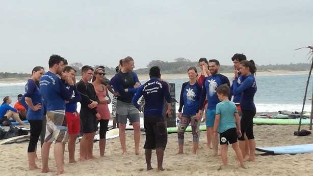 Un grupo de personas en una playa, algunas con camisetas azules con texto en la espalda y otras con ropa informal.