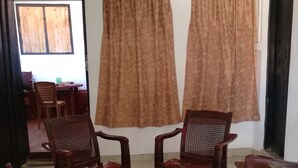 Una habitación con una mesa de comedor y sillas, dos ventanas amplias con cortinas, y una puerta que da a otra estancia.