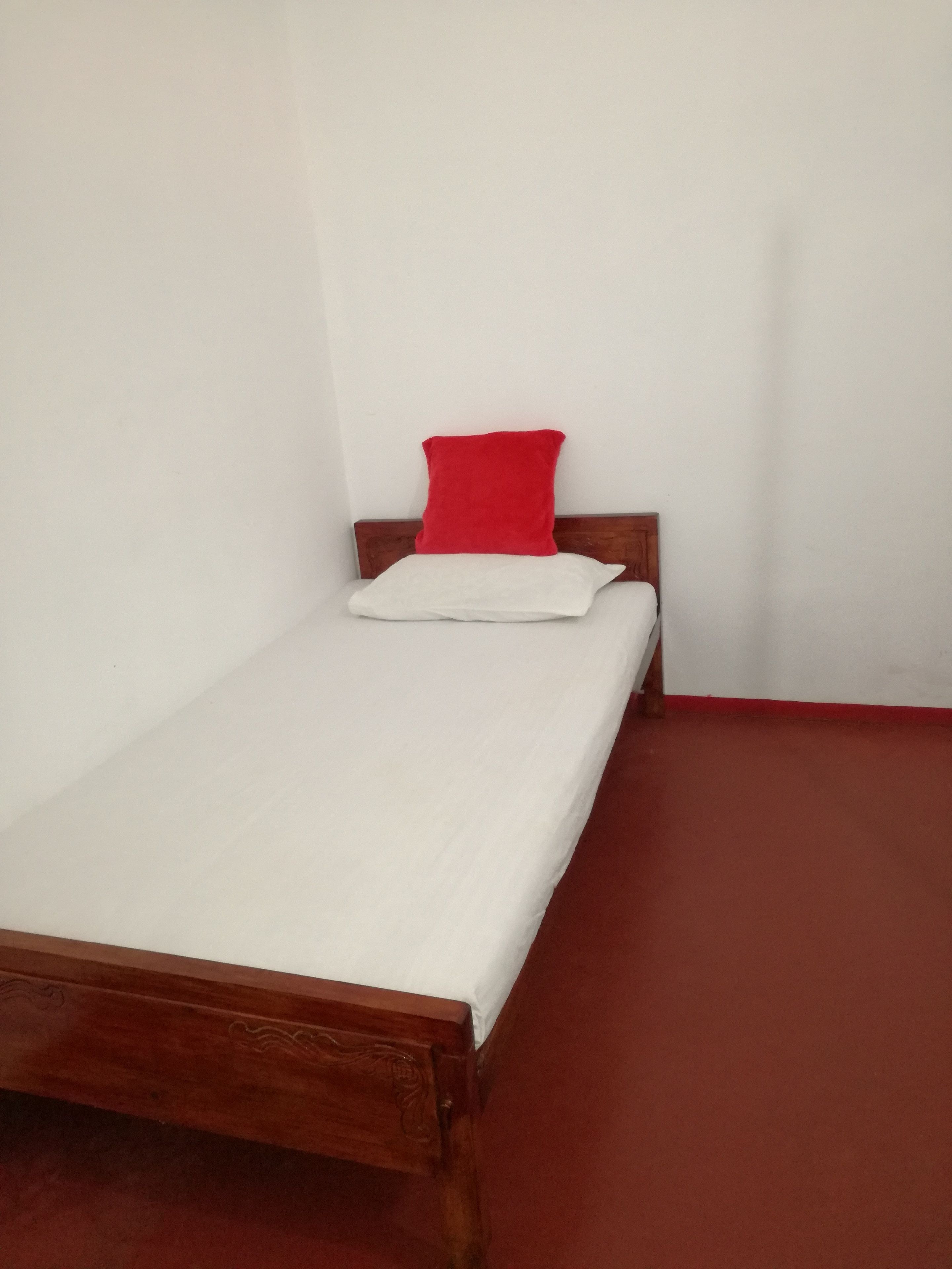 Ein Einzelbett mit hölzernem Gestell und einem roten Kopfkissen.