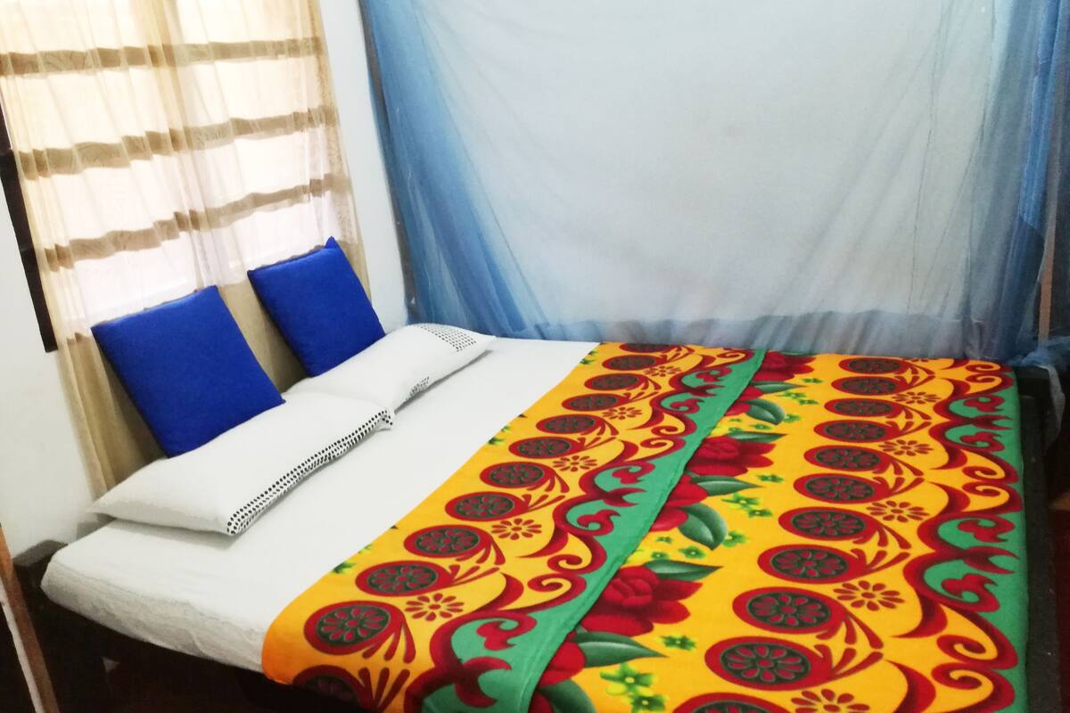 A bed with a colorful bedspread, two blue pillows, and a white mattress cover.