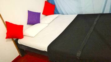 A bed with white and black bedding, red and purple pillows, and a blue sheer curtain.
