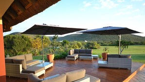 An outdoor patio with wicker furniture, two large umbrellas, and a view of a green landscape with hills. - ParkView Lodge (Colchester)