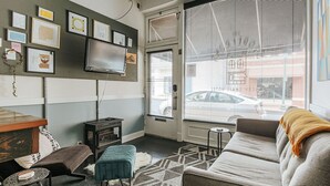 A cozy living room with a sofa, a small coffee table, and a TV mounted on the wall. - The Storefront (Staunton)