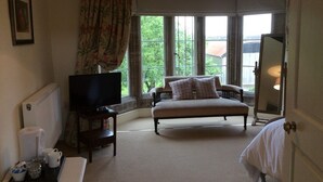 A hotel room with a bed, a TV, a small table with a tray of items, and a window with curtains.