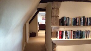 A narrow hallway with a bookshelf filled with books, a stone pillar, and a carpeted floor.