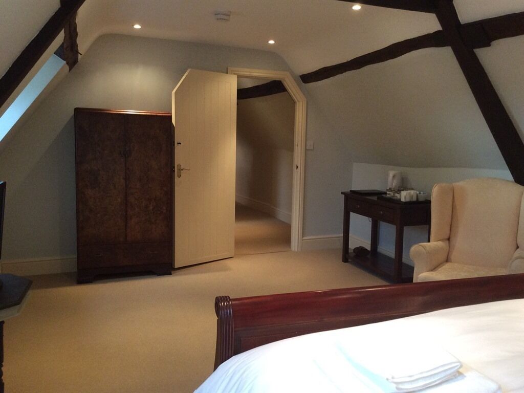 A bedroom with a large bed, a chair, a desk, and a wardrobe.