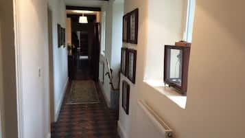A narrow hallway with patterned flooring, framed pictures on the walls, and a radiator on the right.