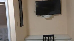 Une pièce avec un bureau blanc, une chaise noire et un téléviseur fixé au mur.