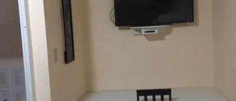 A room with a white desk, a black chair, and a mounted television on the wall.