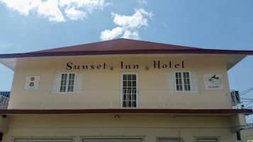 The exterior of the Sunset Inn Hotel with a red roof, two windows with shutters, and a sign indicating the hotel's name.
