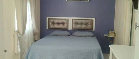 A bedroom with a bed, an air conditioner, a bedside table, and a curtain.