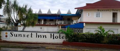 Exterior del hotel Sunset Inn, con un letrero, techo rojo y toldo azul.