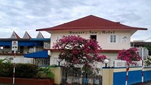 Un bâtiment portant l’inscription « Sunset Inn Hotel », avec un toit rouge, entouré de plantes à fleurs roses et d’une clôture bleue.