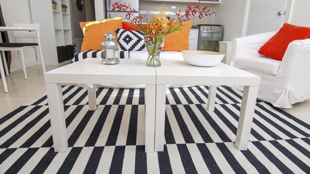 A modern kitchen with white cabinets, a microwave, and a stove. There is a white dining table with a black and white striped rug. - Ratho Mill Apartments (Ratho Mill)
