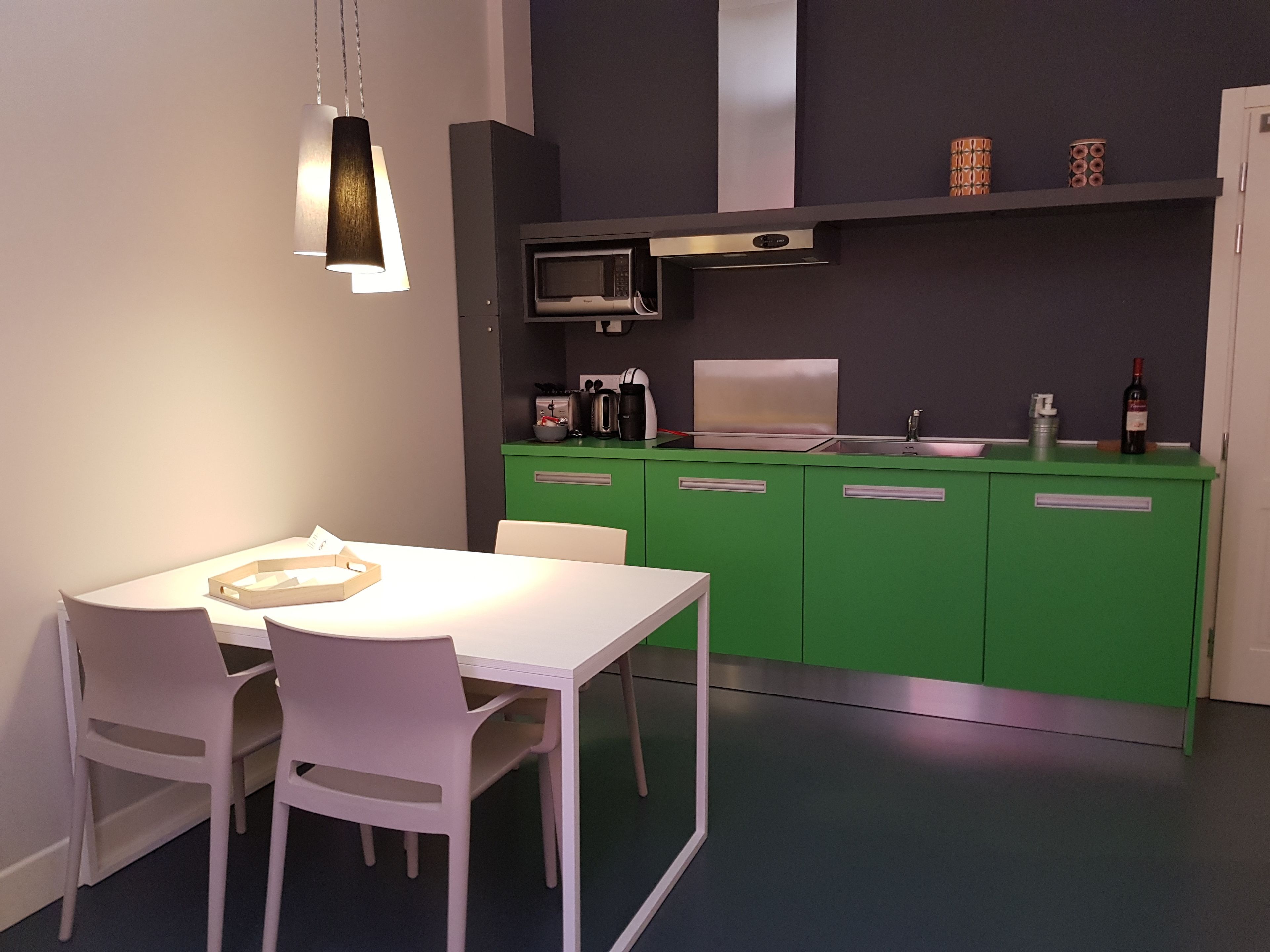 Une cuisine moderne avec des meubles de couleur verte, une table à manger blanche et des chaises.