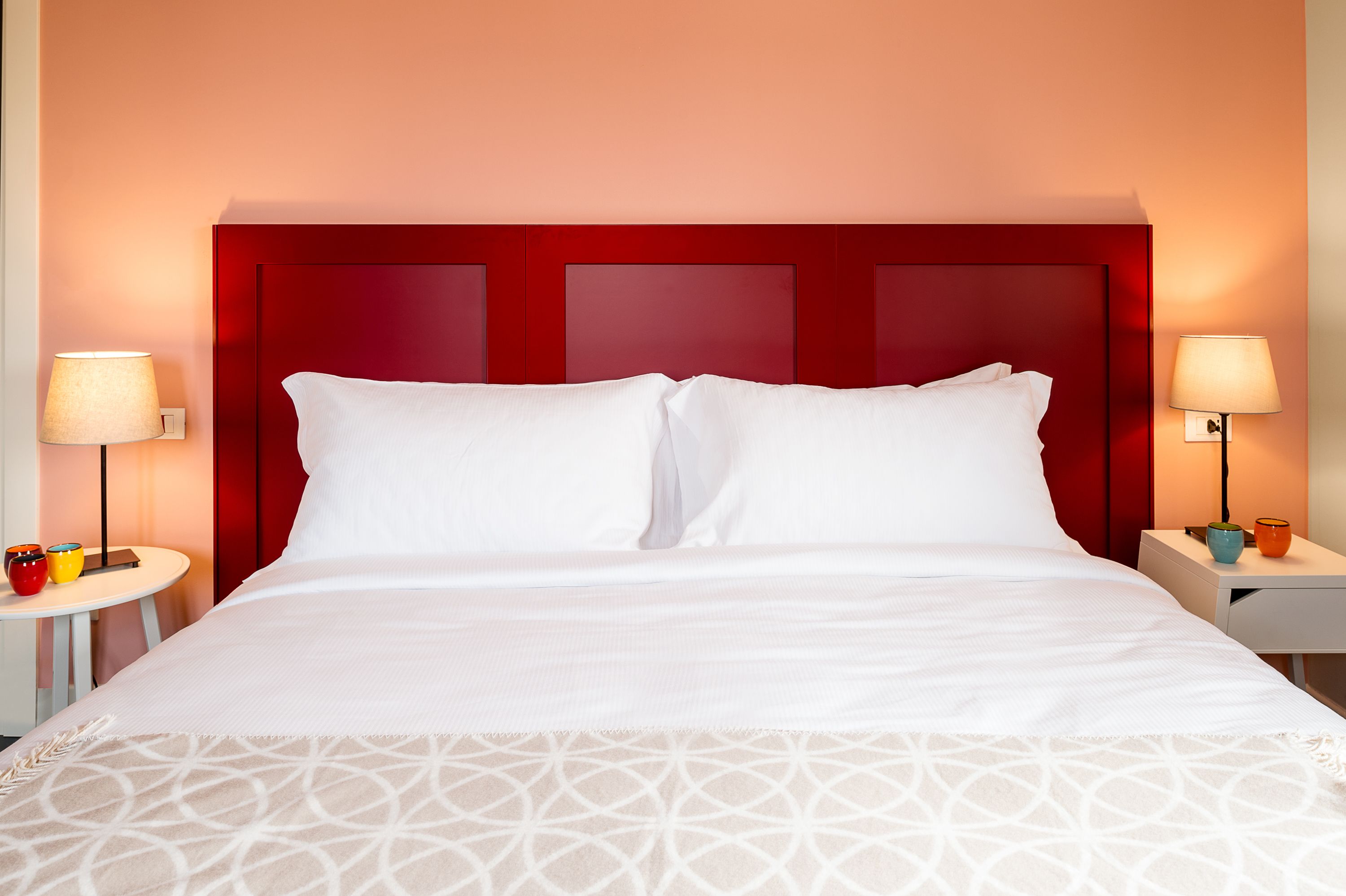 A hotel room with a large bed, two bedside tables, and a red headboard.