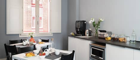 Una cocina moderna con armarios blancos, una cafetera y un comedor con una mesa preparada para dos.