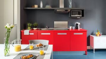 A modern kitchen with red cabinets, a microwave, and a coffee maker. There is a dining table with breakfast items and a vase of flowers.