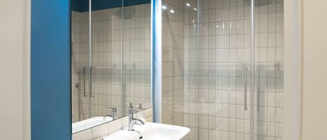 Une salle de bain moderne avec une douche à parois de verre, un lavabo blanc et un miroir.