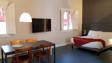 A room with a bed, a dining table with chairs, a TV, and a window with curtains.