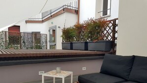 A modern outdoor seating area with a wooden bench and a small white table, a potted plant, and a staircase leading to an upper level. - Almarossa (Bologna)