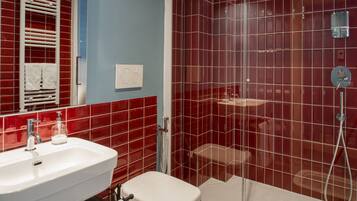 A bathroom with a white sink, a toilet, and a shower with red tiles.