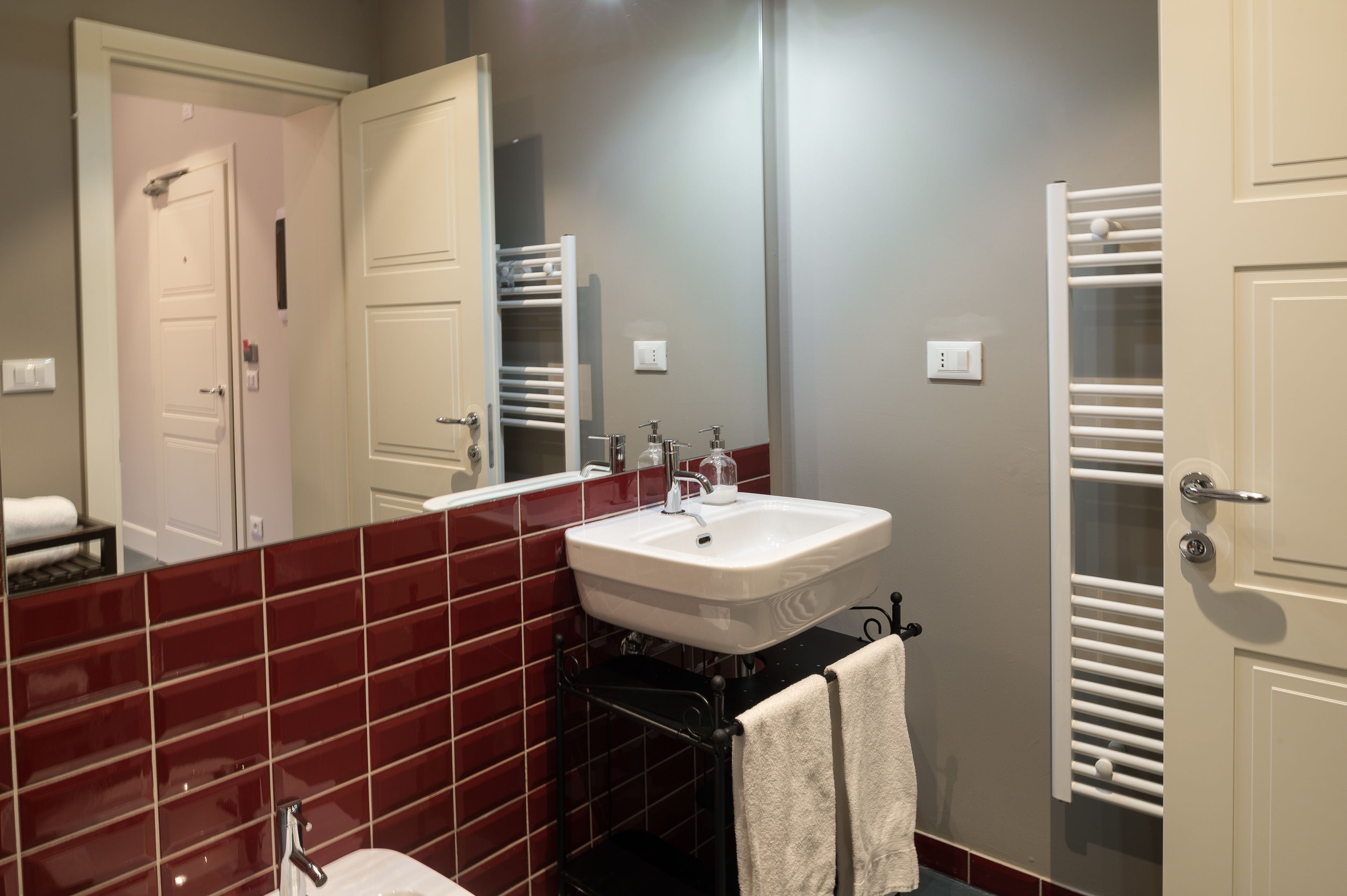 A bathroom with a white sink, red-tiled walls, and a towel rack.