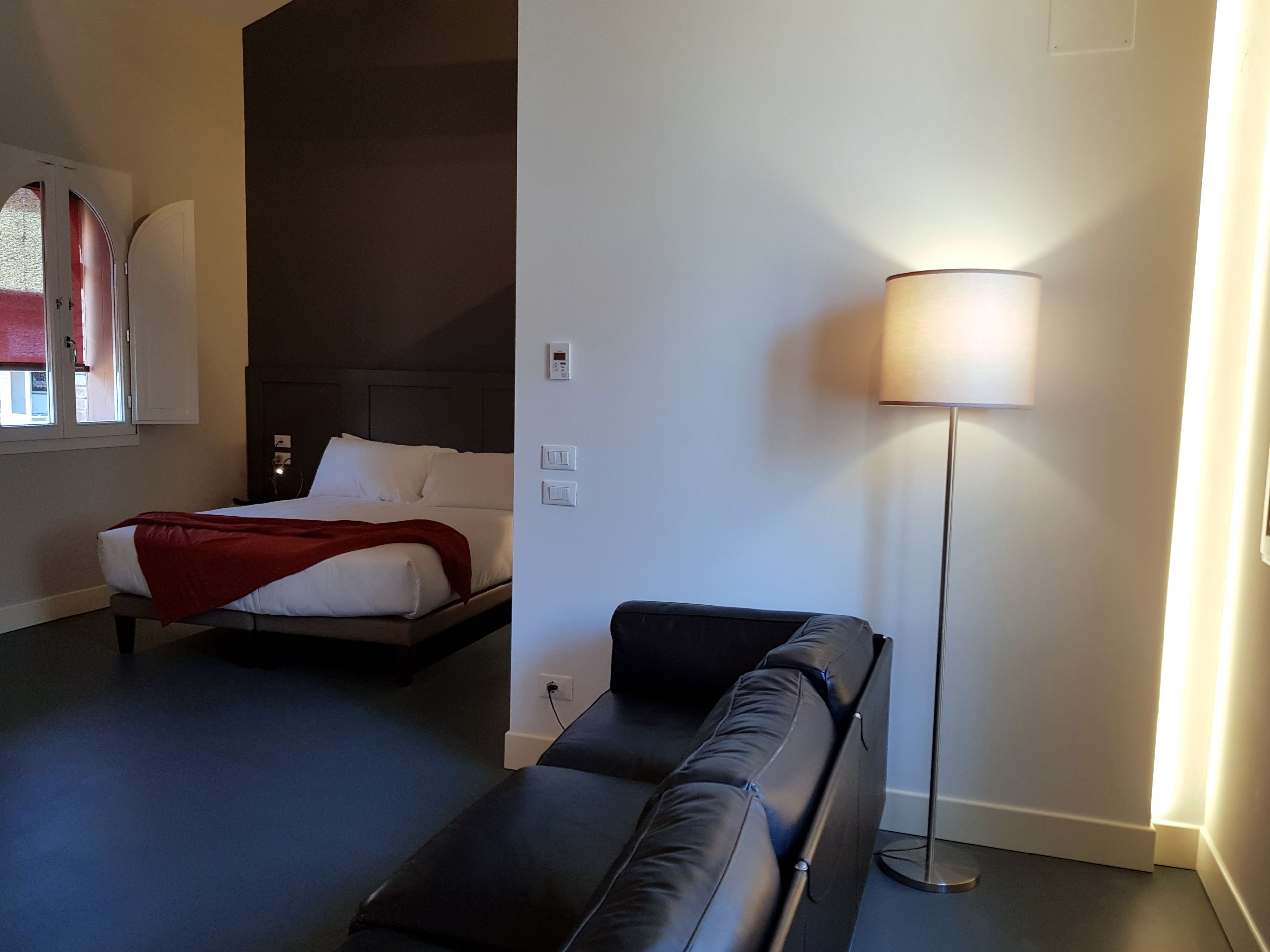 A hotel room with a bed, a bedside table, a lamp, and a sofa.