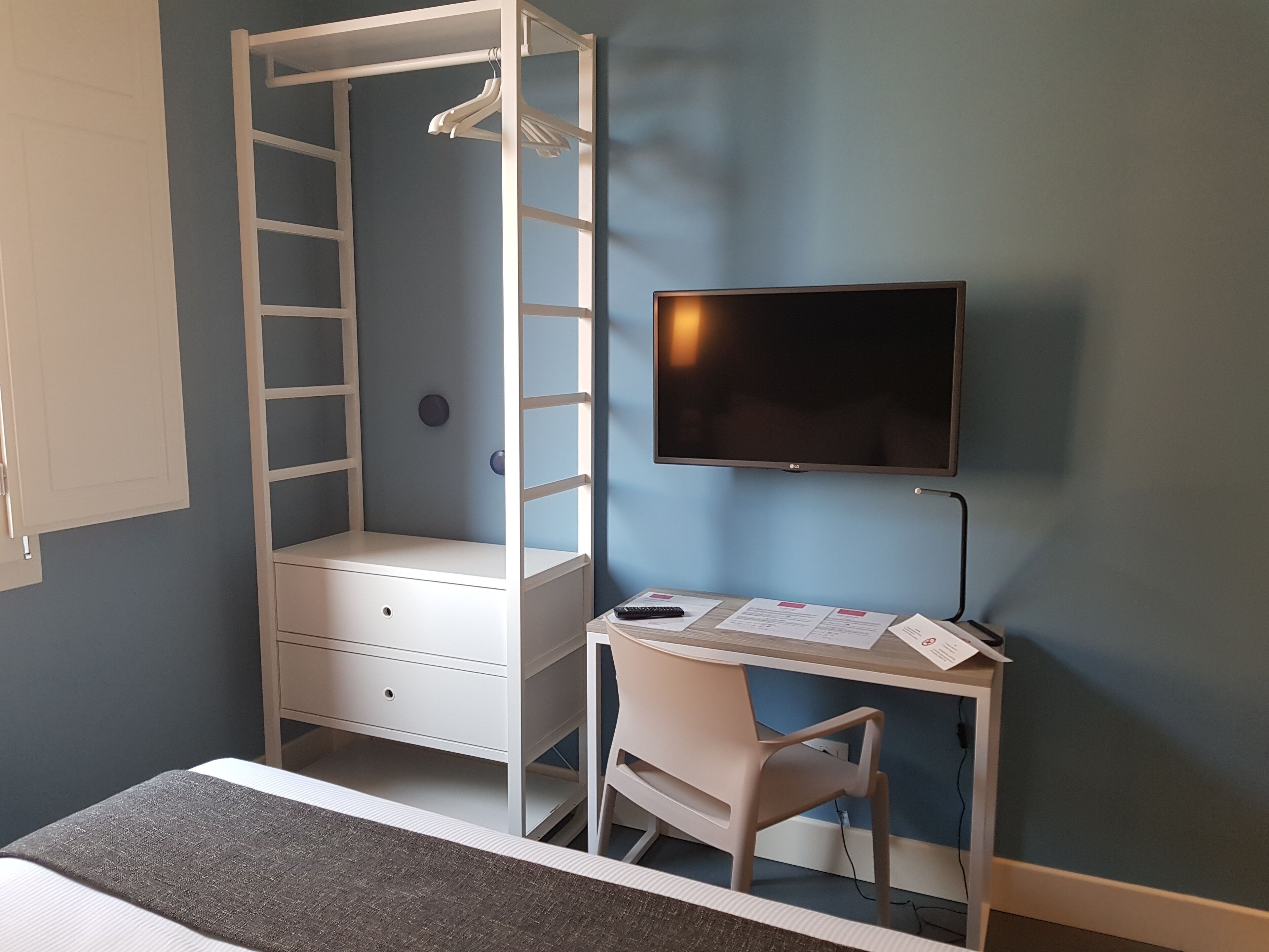 A bedroom with a bed, a desk with a chair, a TV, and a wardrobe with a ladder.