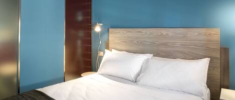 Un lit bien fait, avec du linge de lit blanc et des oreillers, une tête de lit en bois et une table de chevet avec une lampe.
