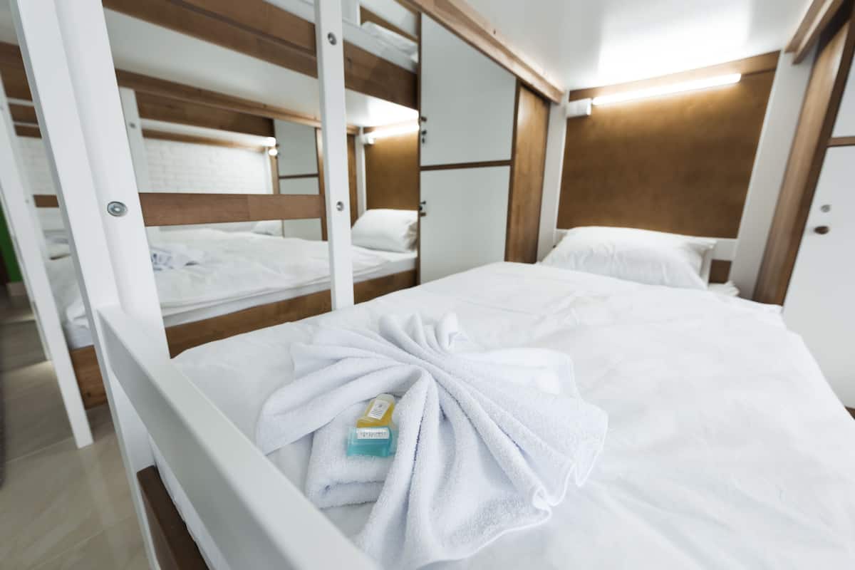 A bunk bed room with white bedding and a neatly folded towel on the lower bunk.