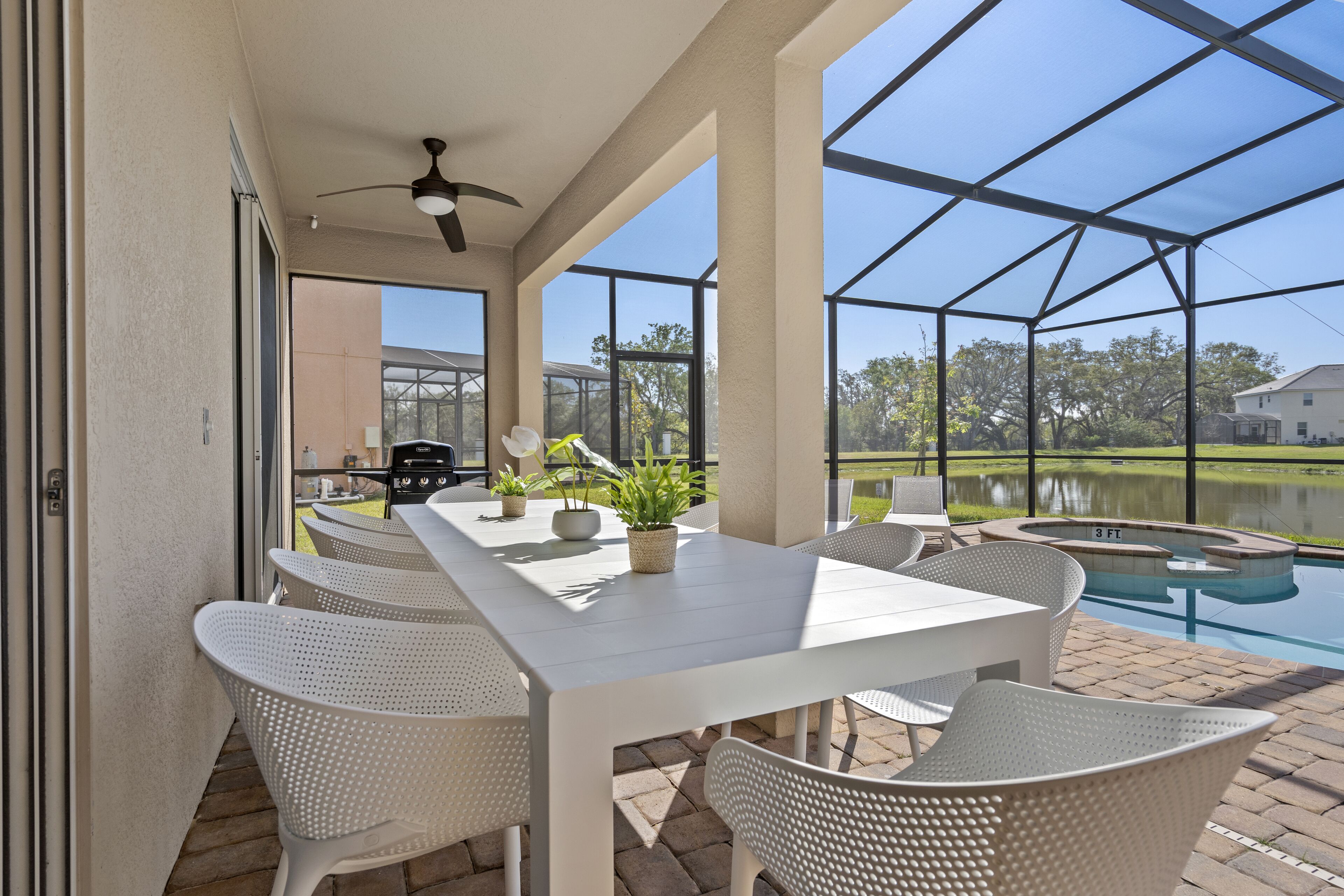 A covered patio with a pool, white table and chairs, and potted plants.