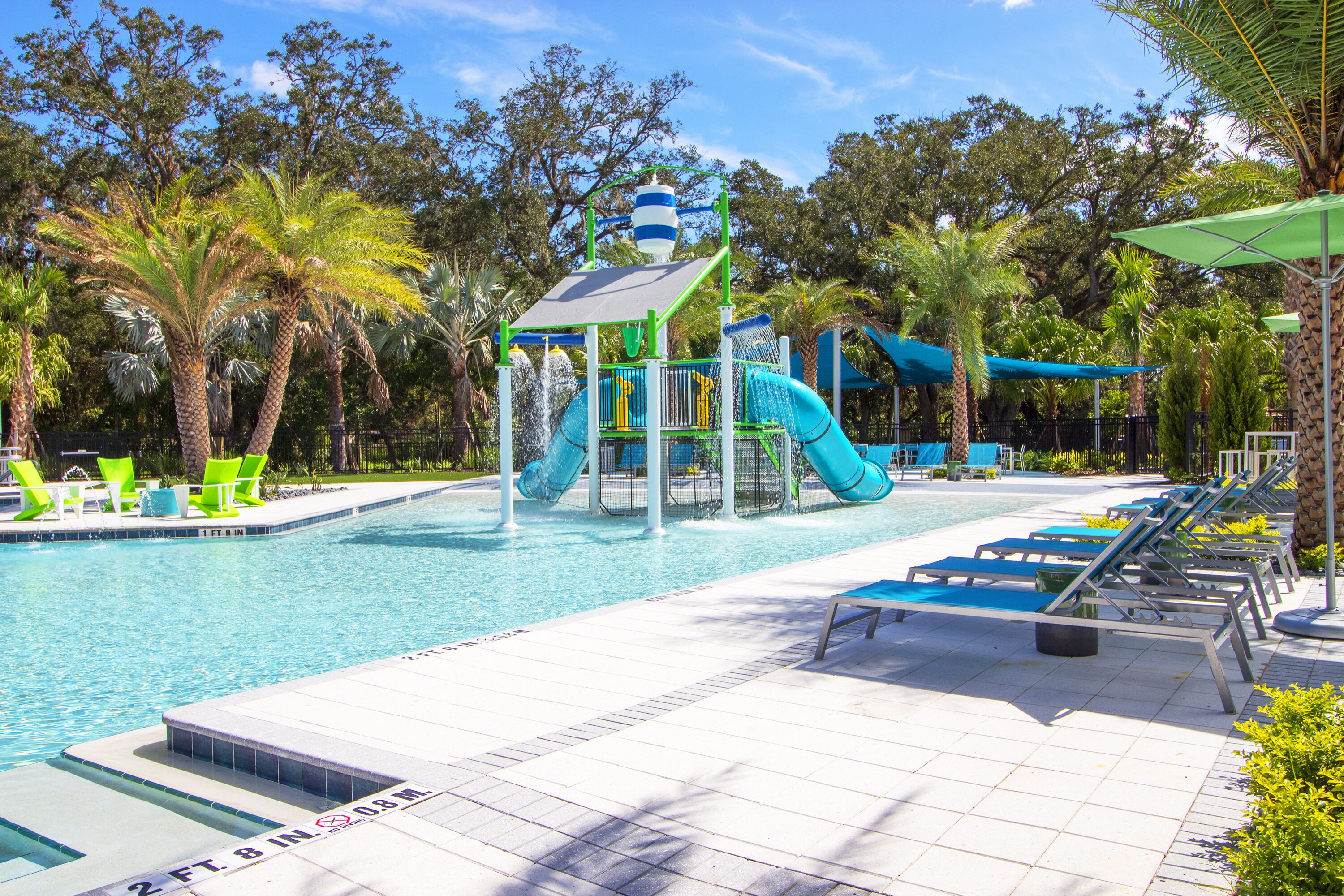 A swimming pool with a water slide, lounge chairs, and palm trees.