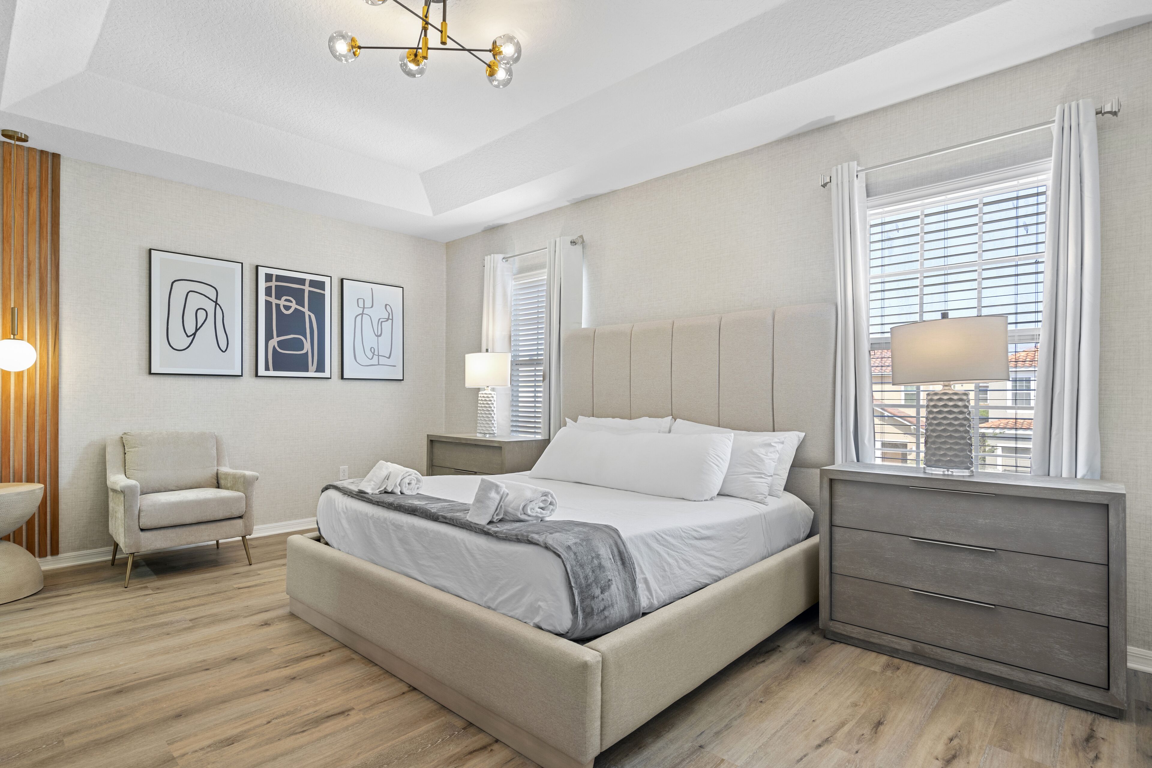 A modern bedroom with a bed, bedside tables, a chair, and artwork on the wall.