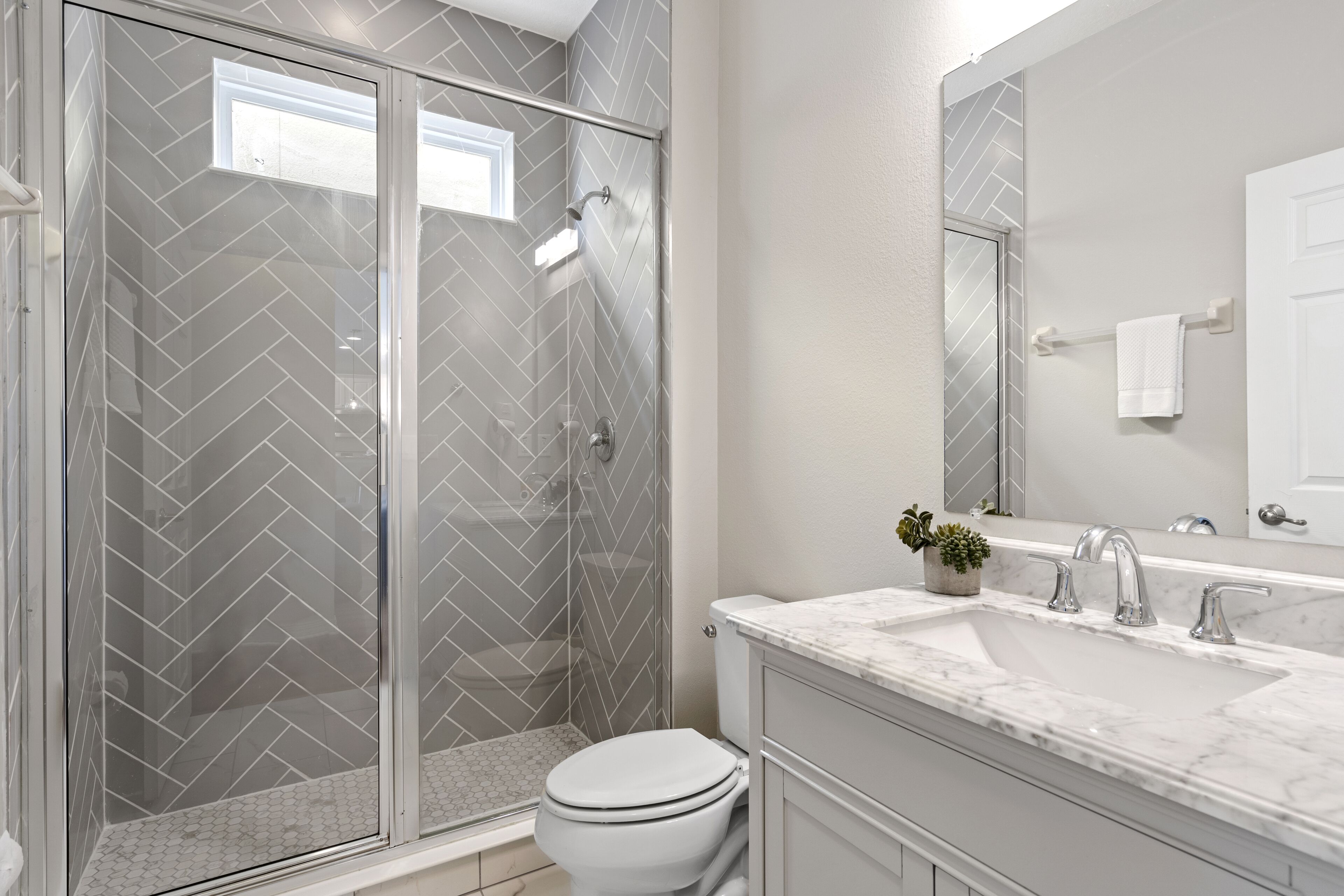 A modern bathroom with a glass-enclosed shower, a white toilet, and a marble sink.