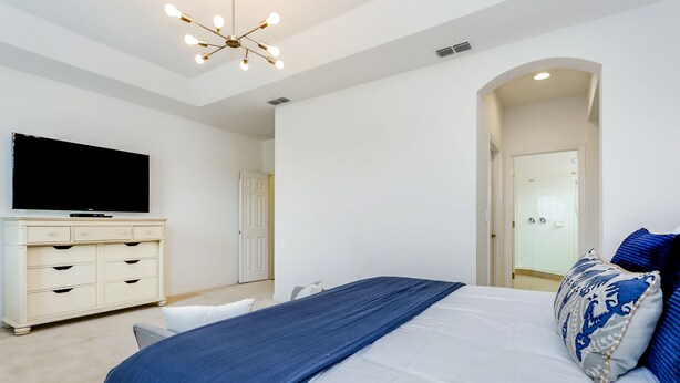 A bedroom with a large bed, a TV, a dresser, and a door leading to another room.
