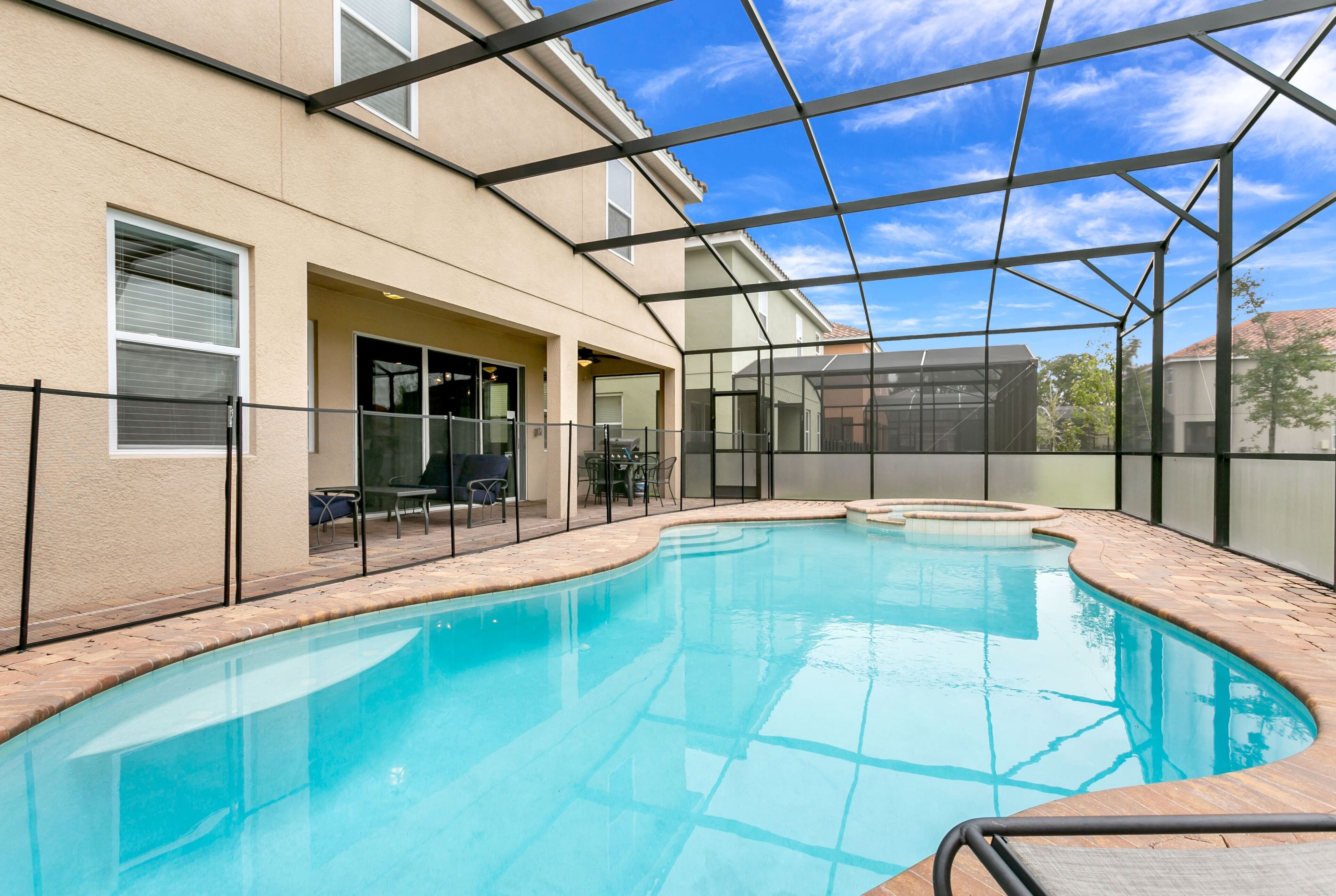 A swimming pool with a glass enclosure, a patio area with outdoor furniture, and a clear blue sky.