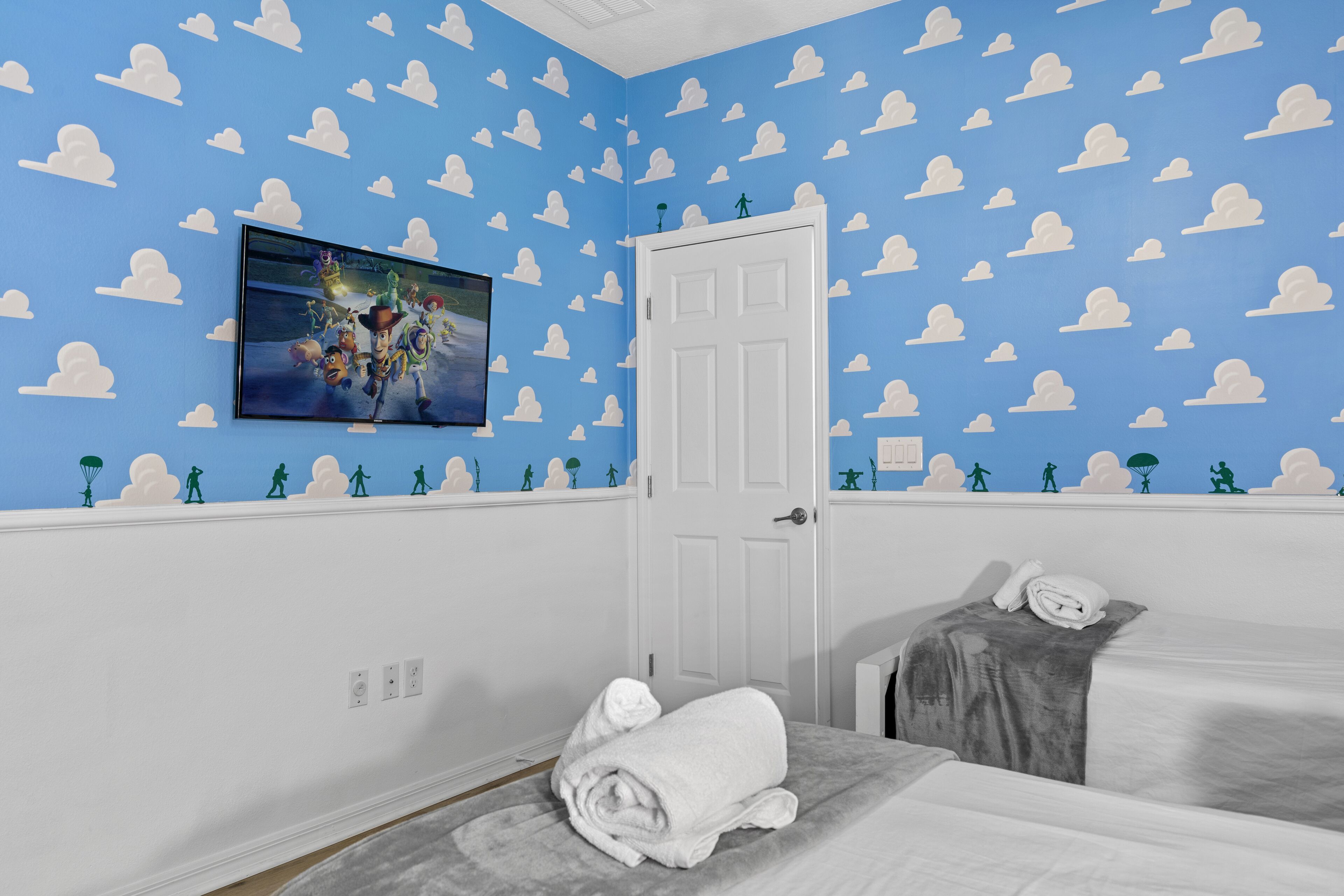 A room with a blue wall featuring white cloud patterns, a white door, and a bed with a gray blanket.