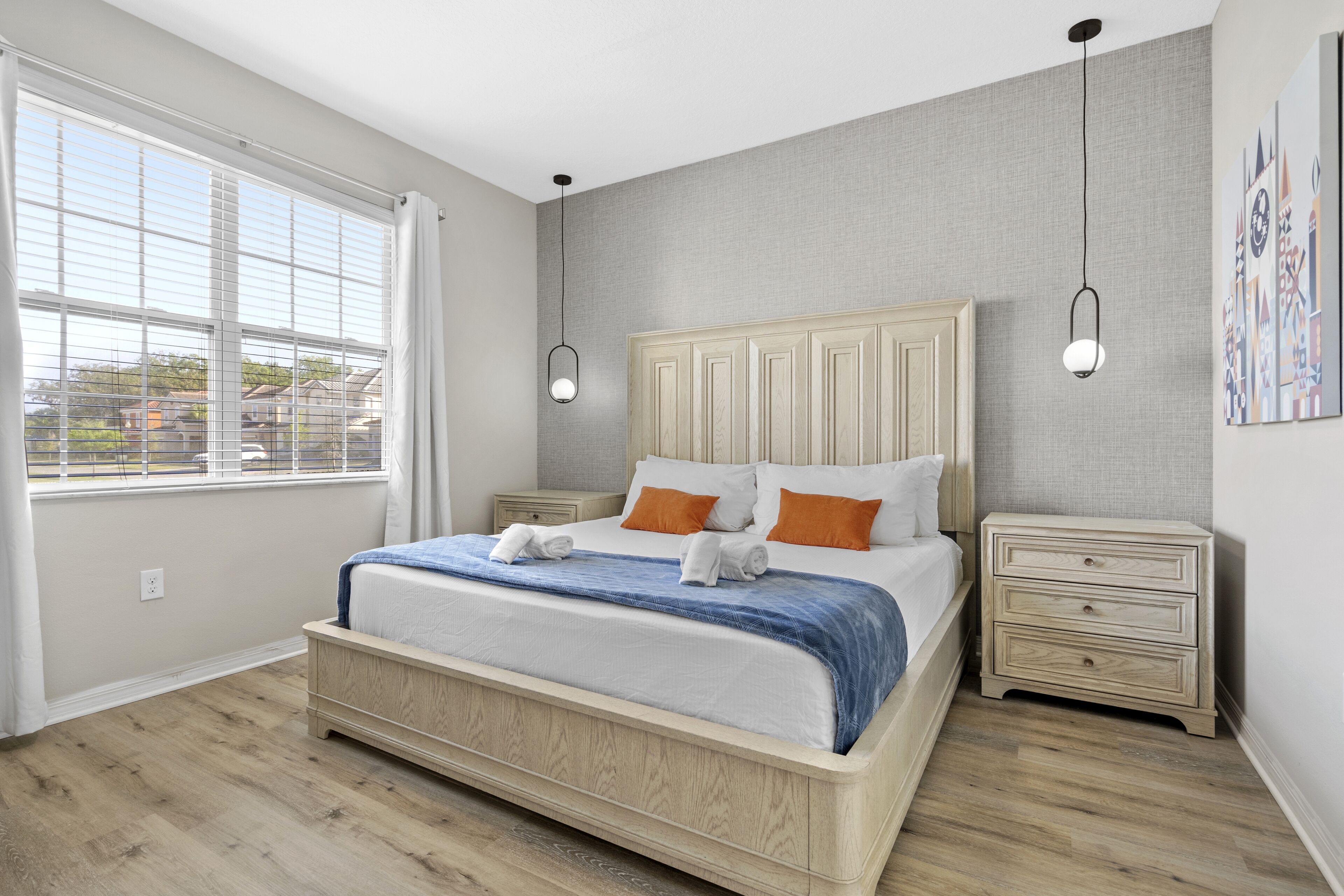 A bedroom with a large bed, bedside tables, a window with blinds, and a view of the outside.