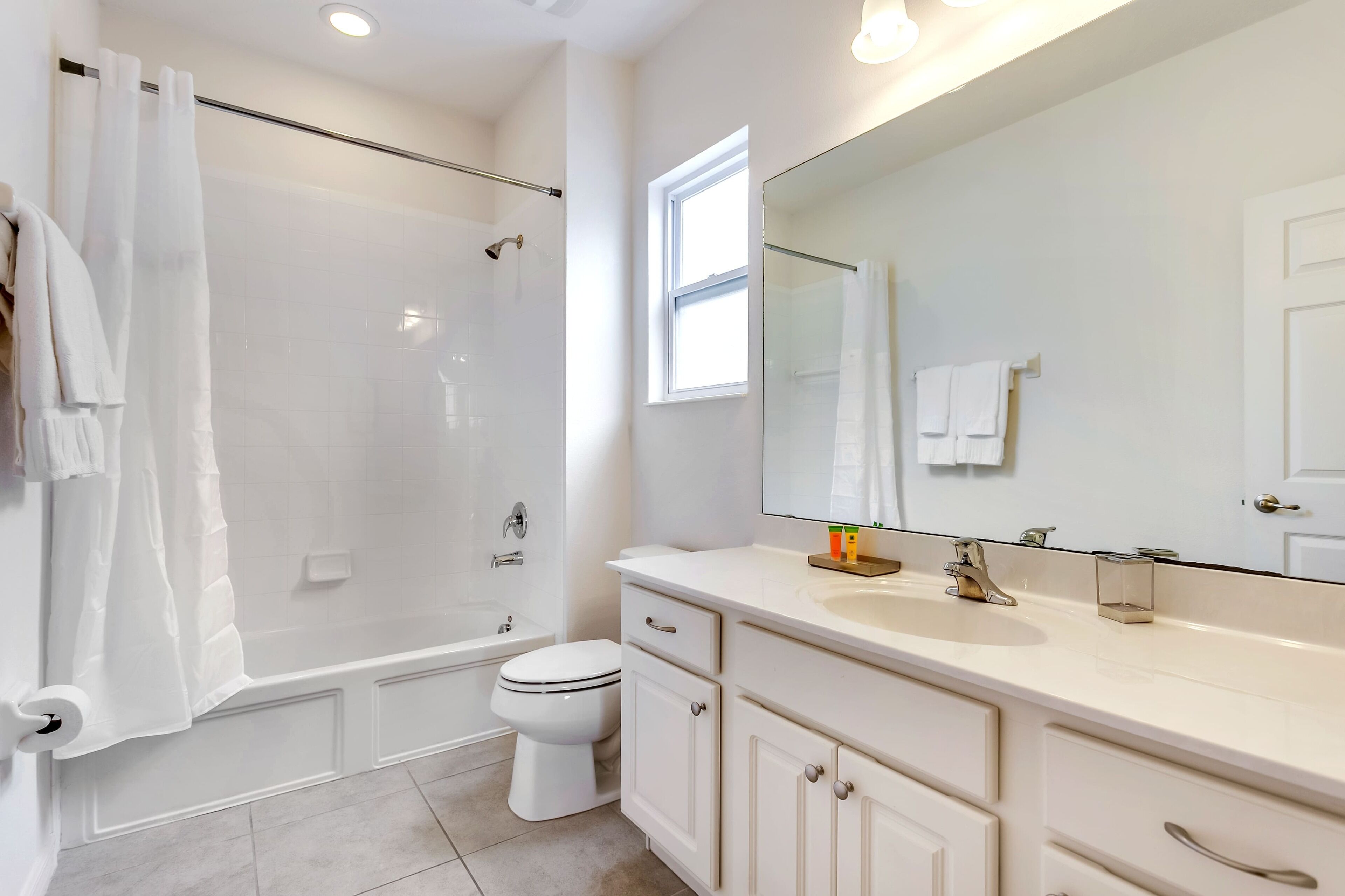 A modern bathroom with a glass shower enclosure, a toilet, a sink with a large mirror, and a window providing natural light.