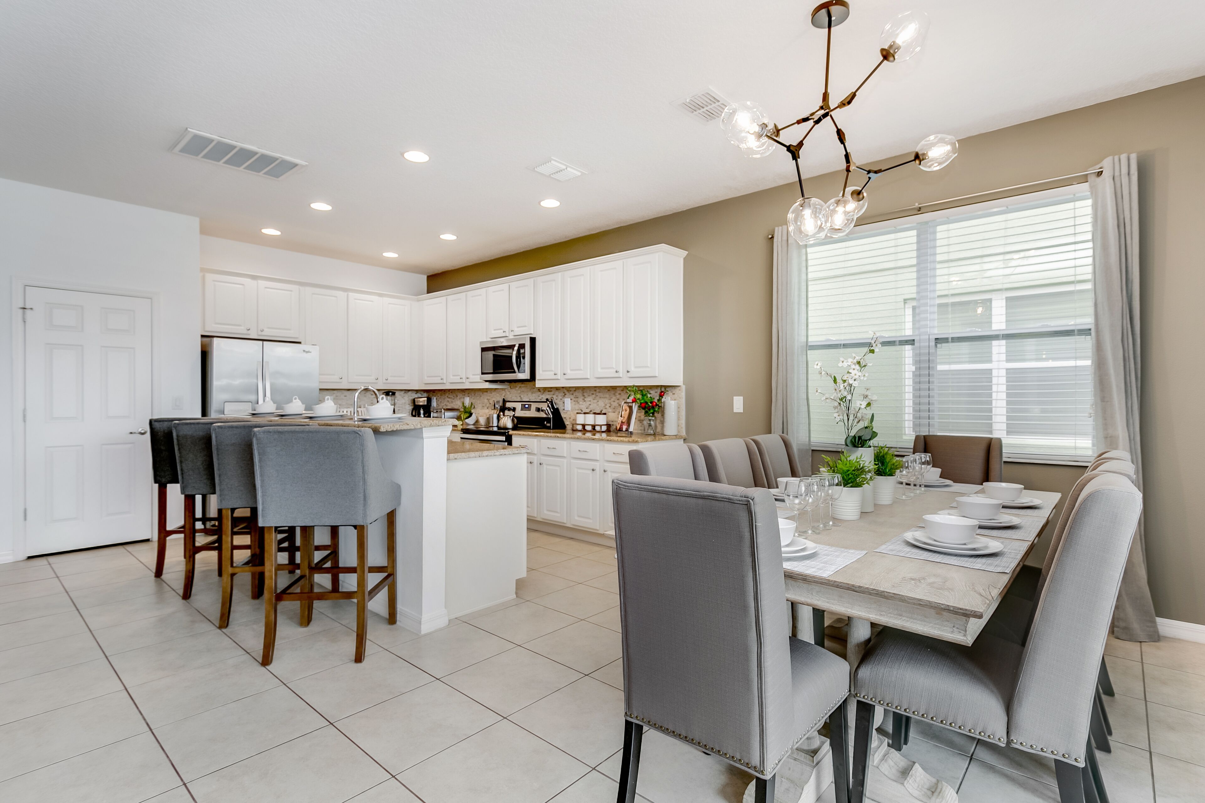 A modern kitchen with white cabinets, a central island, and a dining area with a table set for six.