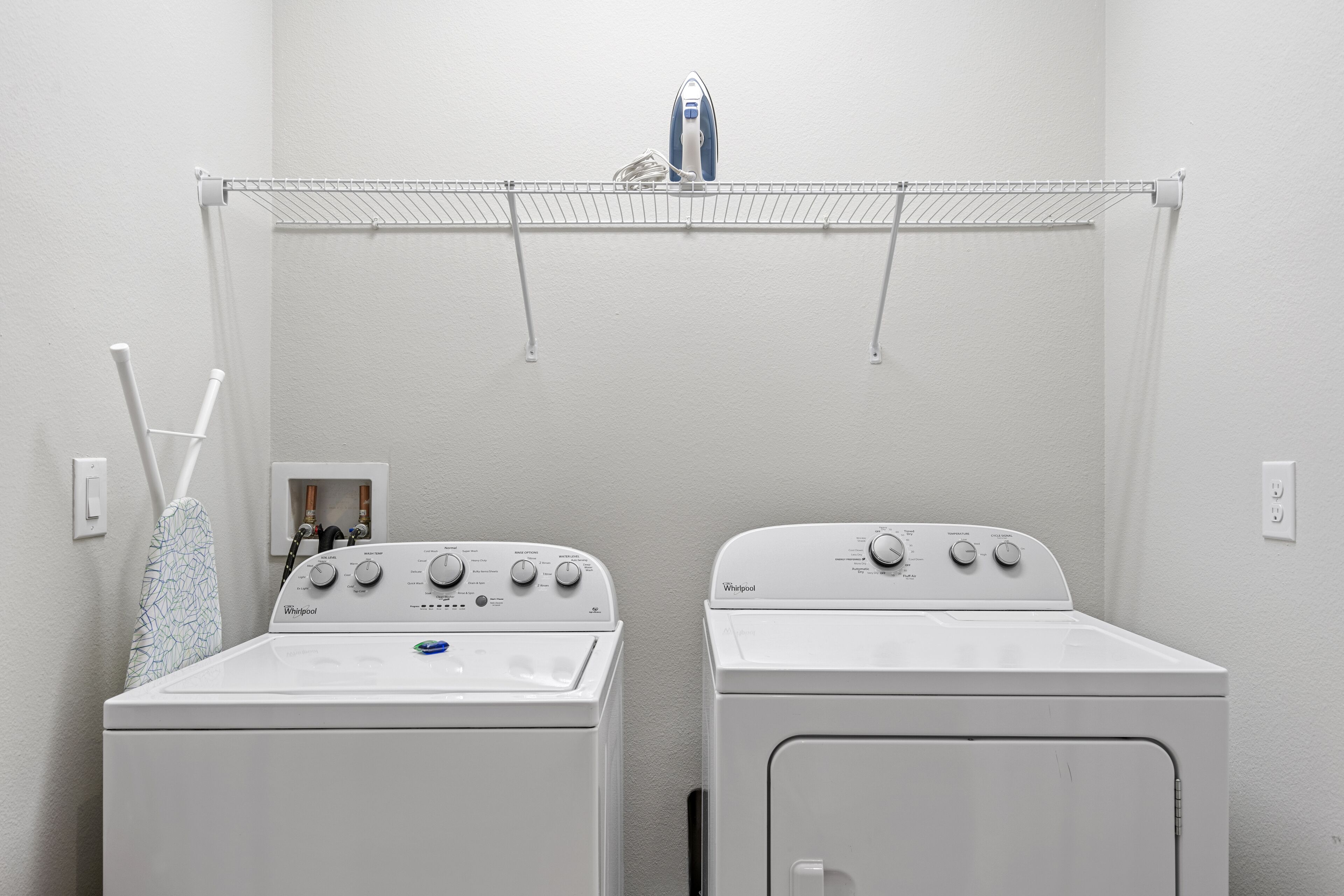A laundry area with two white Whirlpool washers and a drying rack above.