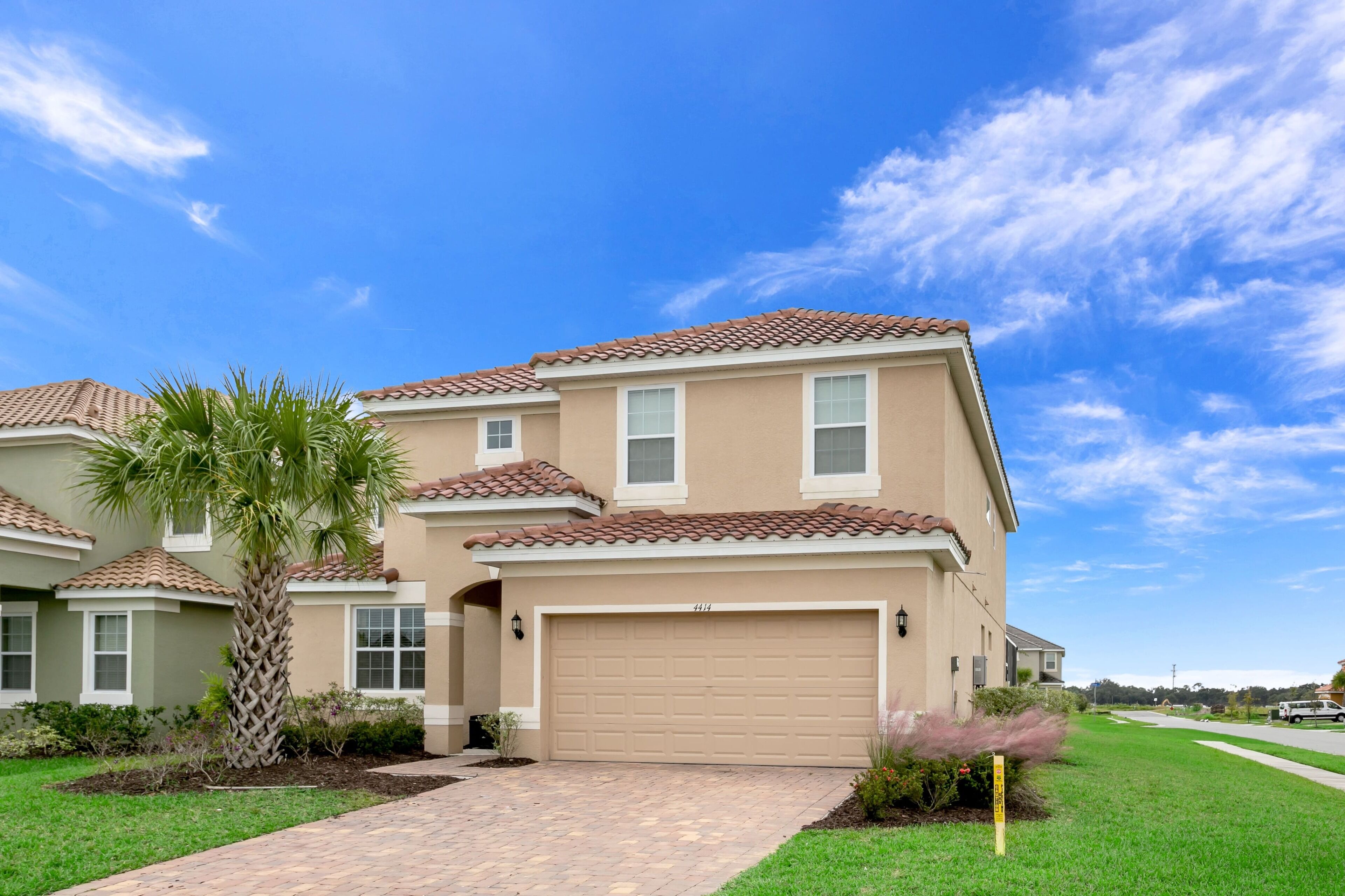 A two-story house with a beige facade, a brown tiled roof, and a garage.