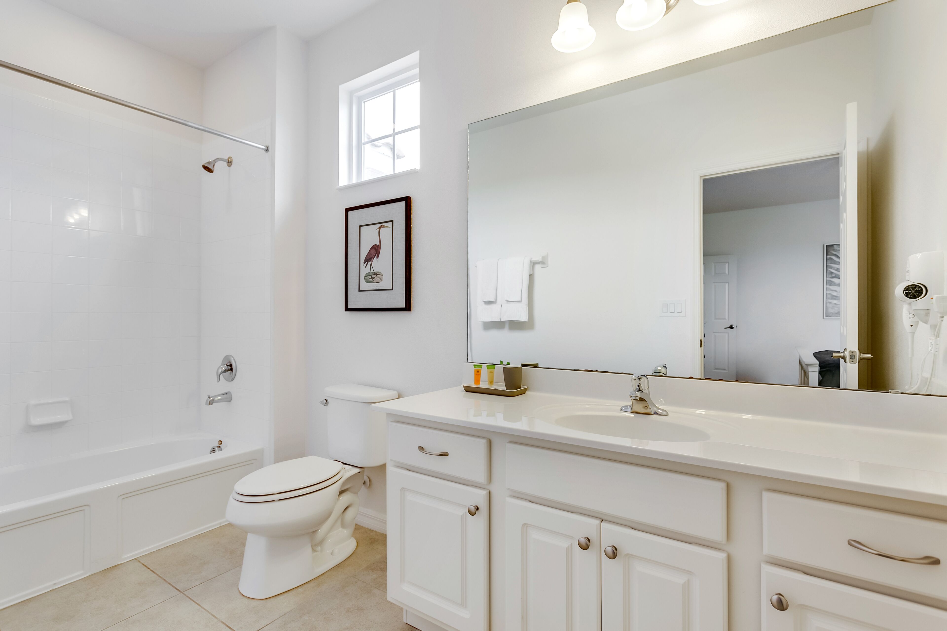 A bathroom with a bathtub, toilet, and a large mirror above the sink.