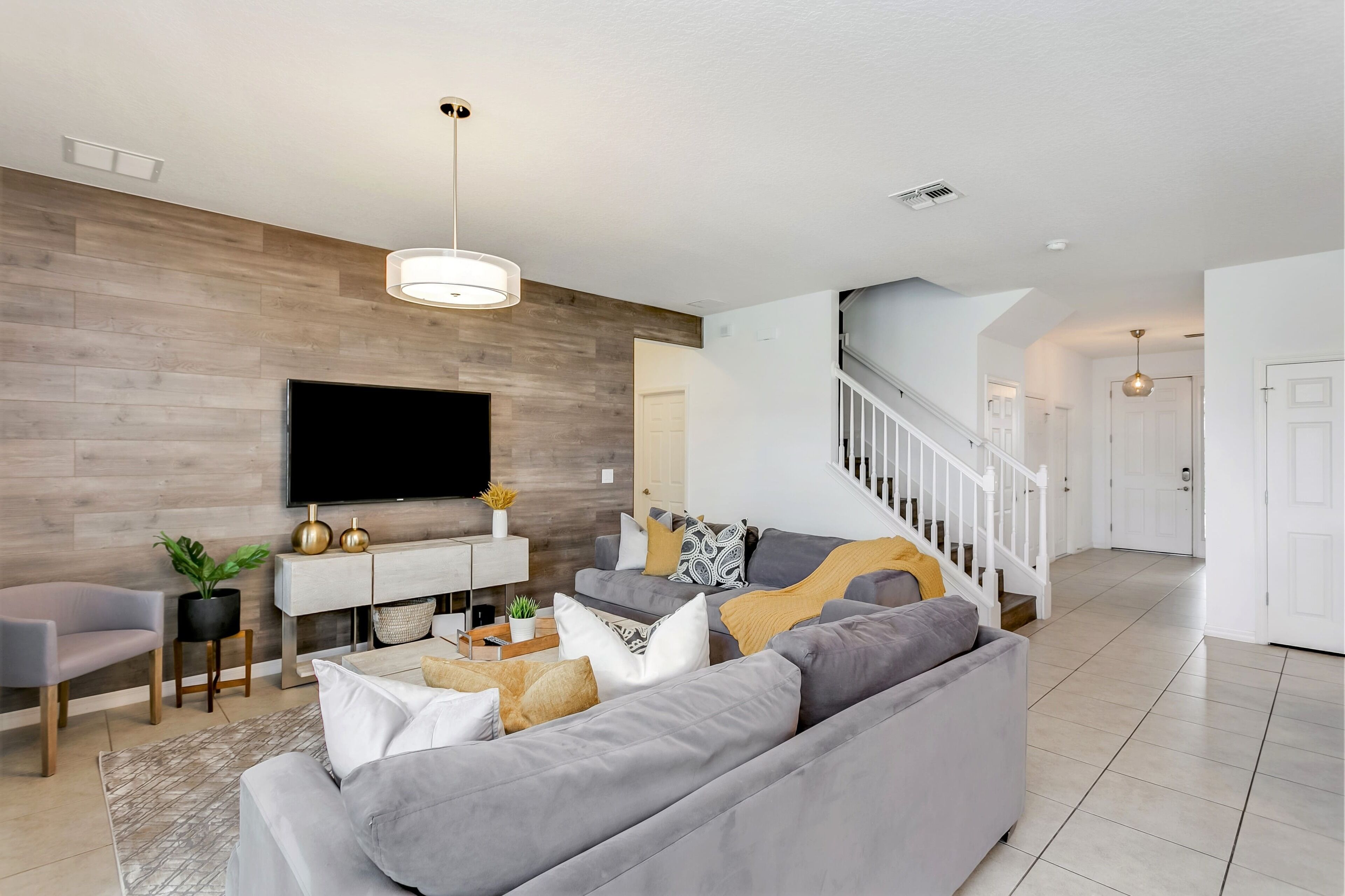 A modern living room with a flat-screen TV, grey sofas, and a staircase leading to another level.