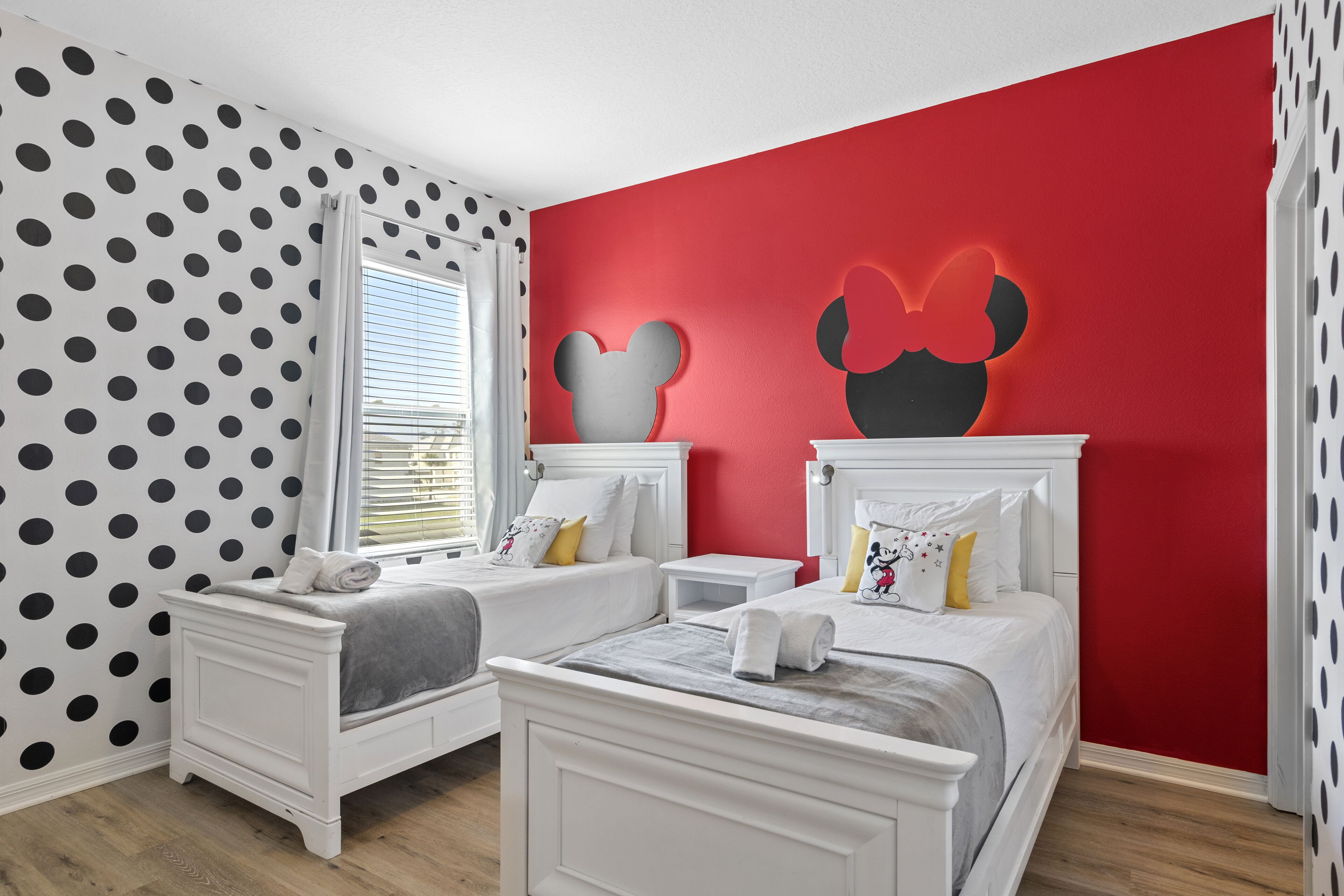 Un dormitorio con dos camas, una pared de acento roja y decoración de Mickey Mouse.