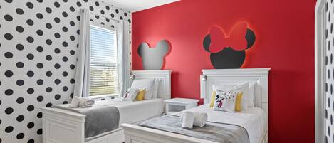 Un dormitorio con dos camas, una pared de acento roja y decoración de Mickey Mouse.