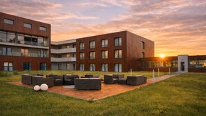 A modern building with multiple floors and large windows, surrounded by a grassy area with outdoor seating. - Santé Royale Hotel & Gesundheitsresort Bad Langensalza (Bad Langensalza)