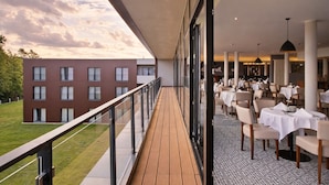 A modern outdoor dining area with a wooden deck, glass railings, and tables set for dining. - Santé Royale Hotel & Gesundheitsresort Bad Langensalza (Bad Langensalza)